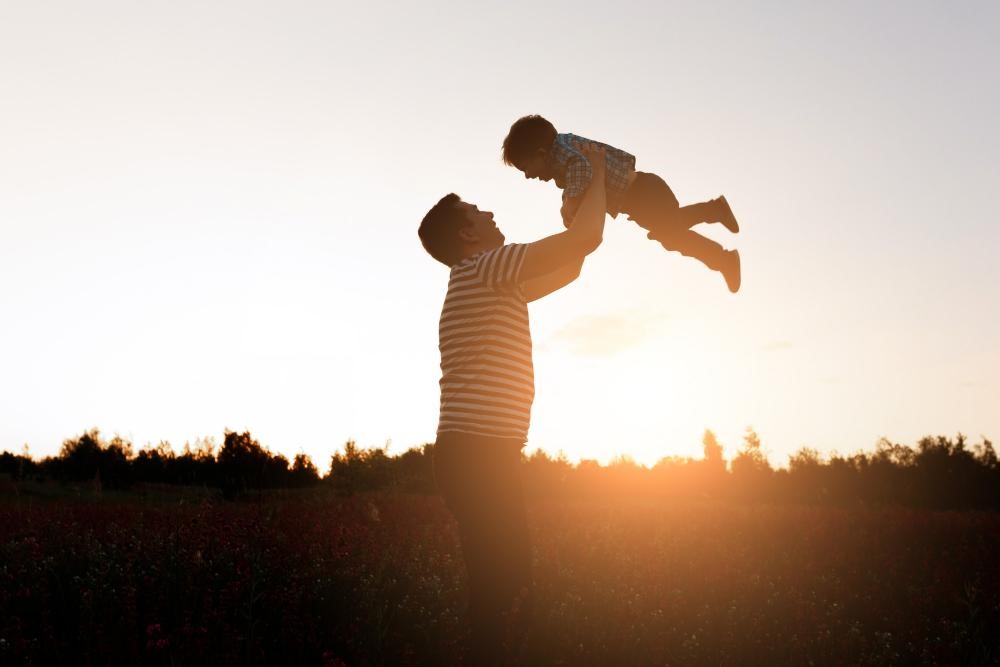 Imagem de um pai levantando seu filho ao ar durante o pôr do sol, representando diferentes tipos de pai e a importância da paternidade na formação emocional das crianças