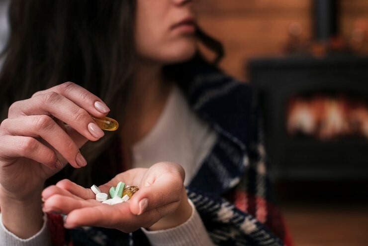 Mulher segurando comprimidos na mão, preparando-se para tomar um remédio para enxaqueca, em um ambiente aconchegante com uma lareira ao fundo.